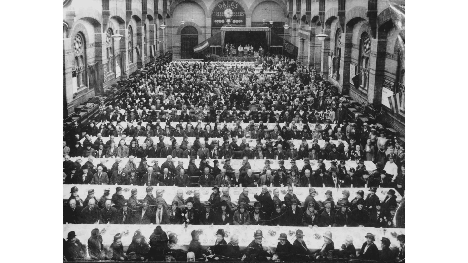 An old black and white photograph inside the Corn Exchange taken from above. There are rows and rows of white cloth tables completely covering the hall, and over 500 people sat down at them awaiting food. They are dressed formally.