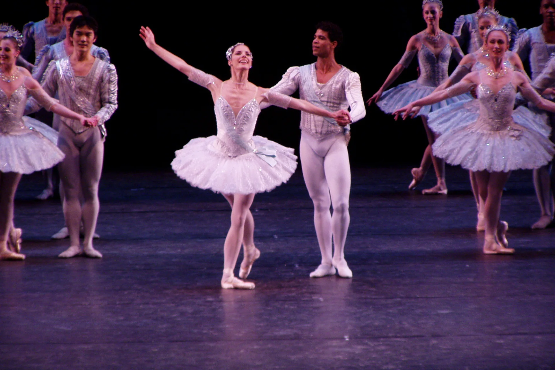 Image shows coloured photographic image of Darcey Bussell performing on Corn Exchange stage in a ballet production in a light pink tutu. She is being held at the waist and looks as is about to be lifted up in the air by a male dancer.